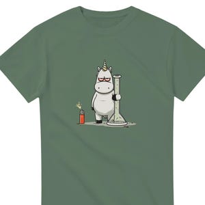 Könnte beinhalten: Grünes T-Shirt mit einem Cartoon-Einhorn, das eine Bong hält und eine Brille trägt. Neben dem Einhorn befindet sich ein rotes Feuerzeug mit einer Flamme. Das Design ist humorvoll.
