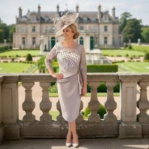 Woman in formal Dress in taupe colour by couture club. standing on a balcony with a grand building and garden
