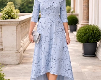 May include: A light blue dress with a floral pattern and a matching hat. The dress has a high-low hemline and three-quarter sleeves. The woman is also wearing silver heels and carrying a silver clutch.