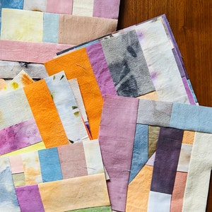 May include: A collection of fabric squares in various shades of pink, purple, blue, orange, yellow, and green. The squares are arranged in a random pattern and have a hand-dyed look.