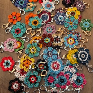 May include: A collection of colorful beaded flower charms with gold-tone lobster clasps. The charms feature various colors, including turquoise, orange, yellow, red, and pink. Each charm is intricately beaded in a floral design, perfect for attaching to keys or bags.