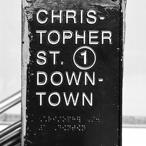 May include: Black and white sign with the text "Chris-topher St. 1 Down-town" in white lettering. The sign has two silver rivets on the top and bottom.