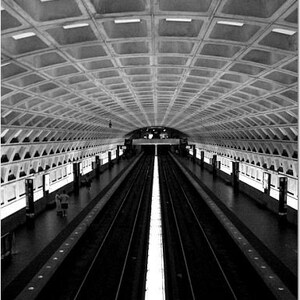 May include: A black and white photo of a subway station with a long, straight tunnel and a white line down the center.