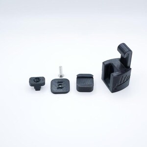 May include: A collection of black 3D-printed components, including a square base with two holes, a small square piece, a screw, a T-shaped piece, and a larger bracket with a curved top. The items are arranged on a white surface.