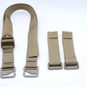 May include: Tan-colored tactical gear straps with metal hardware. The set includes a long, looped strap with a buckle and two shorter straps with buckles. The straps are made of a durable, woven material.