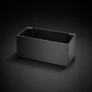 Könnte beinhalten: Ein rechteckiger, mattschwarzer Behälter mit schlichtem, modernem Design. Die Box mit offenem Deckel besteht aus einem soliden Material und steht auf einer dunklen Oberfläche. Die Abmessungen des Behälters betragen ca. 30 cm lang, 15 cm breit und 10 cm hoch.