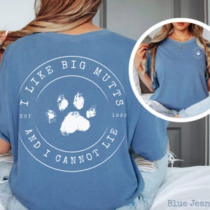 K&ouml;nnte beinhalten: Ein blaues T-Shirt mit einer wei&szlig;en kreisf&ouml;rmigen Grafik auf der R&uuml;ckseite, die in der Mitte einen Pfotenabdruck und den Text I LIKE BIG MUTTS AND I CANNOT LIE EST 1992 zeigt. Auf der Brust befindet sich ein kleineres wei&szlig;es Logo mit Pfote.