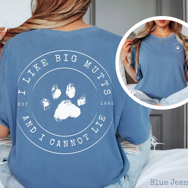K&ouml;nnte beinhalten: Ein blaues T-Shirt mit einer wei&szlig;en kreisf&ouml;rmigen Grafik auf der R&uuml;ckseite, die in der Mitte einen Pfotenabdruck und den Text I LIKE BIG MUTTS AND I CANNOT LIE EST 1992 zeigt. Auf der Brust befindet sich ein kleineres wei&szlig;es Logo mit Pfote.