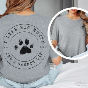 K&ouml;nnte beinhalten: Ein graues meliertes T-Shirt mit einer schwarzen kreisf&ouml;rmigen Grafik auf der R&uuml;ckseite, die in der Mitte einen Pfotenabdruck und den Text I LIKE BIG MUTTS AND I CANNOT LIE EST 1992 zeigt. Auf der Brust befindet sich ein kleines passendes Pfotenlogo.