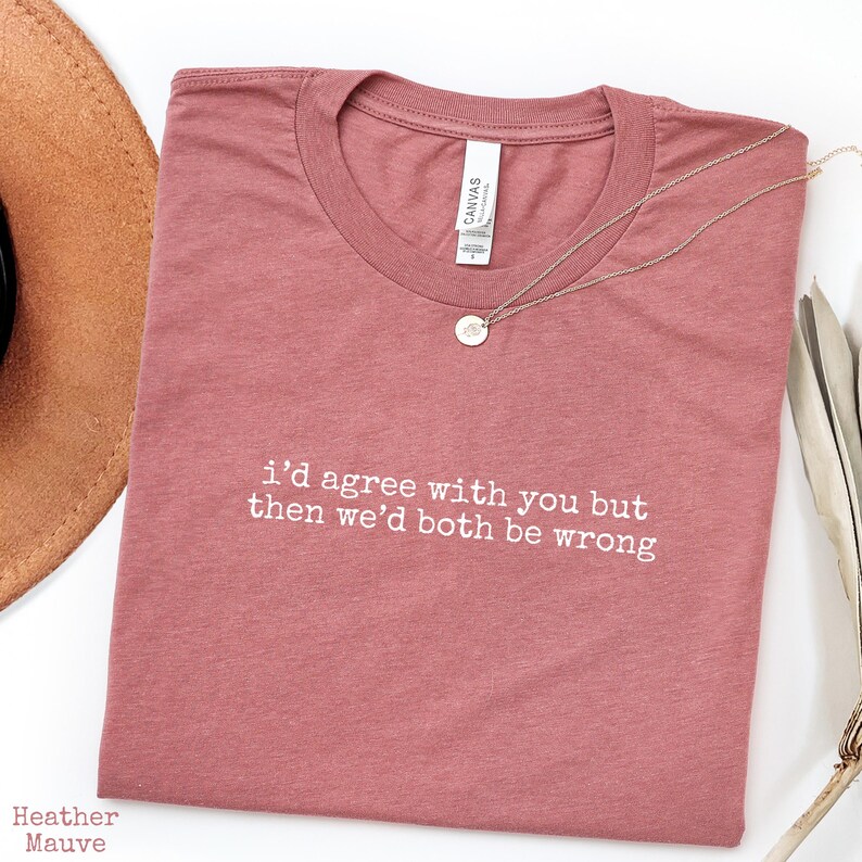 May include: A heather mauve short-sleeve t-shirt featuring the white printed text "i'd agree with you but then we'd both be wrong" centered on the chest. The shirt has a crew neckline and a standard fit, displayed with a delicate silver necklace.