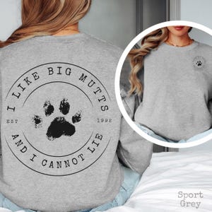 K&ouml;nnte beinhalten: Ein sportgrauer Rundhals-Pullover mit einer gro&szlig;en, kreisf&ouml;rmigen schwarzen Grafik auf der R&uuml;ckseite, die einen Pfotenabdruck in der Mitte und den Text I LIKE BIG MUTTS AND I CANNOT LIE EST 1992 zeigt. Eine kleinere Version ist auf der Brust.