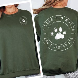 K&ouml;nnte beinhalten: Ein olivgr&uuml;ner Rundhals-Pullover mit einem wei&szlig;en Aufdruck auf der linken Brust und einer gr&ouml;&szlig;eren Version auf der R&uuml;ckseite. Das Motiv ist ein kreisf&ouml;rmiges Emblem mit einem Pfotenabdruck und dem Text I LIKE BIG MUTTS AND I CANNOT LIE.