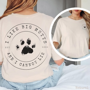 K&ouml;nnte beinhalten: Ein naturfarbenes T-Shirt mit einer schwarzen kreisf&ouml;rmigen Grafik auf der R&uuml;ckseite, die einen Pfotenabdruck in der Mitte und den Text I LIKE BIG MUTTS AND I CANNOT LIE EST 1992 zeigt. Auf der Brust befindet sich eine kleinere Version der Grafik.