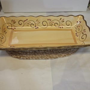 May include: A rectangular ceramic serving tray with a scalloped edge, featuring a cream-colored base with a painted border of brown swirling vines, green leaves, and small dark red berries. The tray has a smooth, glossy finish and a brown rim.