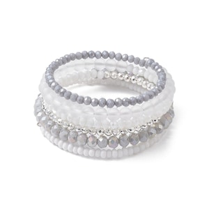 May include: A set of six layered bracelets with white and gray beads. The bracelets are made of different sizes and shapes of beads, creating a layered and textured look.