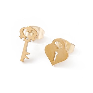 May include: Gold-colored stud earrings featuring a key and a heart-shaped lock design. The key has a decorative top and a detailed key bit. The heart-shaped lock has a keyhole. The earrings are set against a white background.