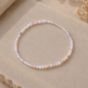 May include: A delicate bracelet composed of small, faceted, translucent beads in soft shades of pale pink, white, and light gray. The circular strand features a repeating pattern of these tiny, polished stones, creating a subtle shimmer.