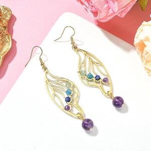 Puede incluir: Pendientes de oro con un delicado dise&ntilde;o de ala y detalles de piedras preciosas de colores. Los pendientes presentan una piedra de amatista colgante en la parte inferior.