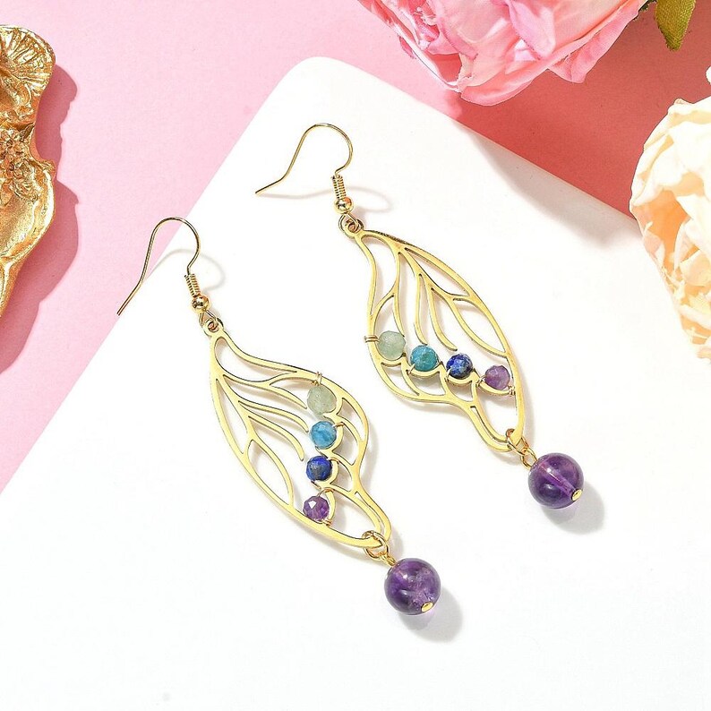 Puede incluir: Pendientes de oro con un delicado dise&ntilde;o de ala y detalles de piedras preciosas de colores. Los pendientes presentan una piedra de amatista colgante en la parte inferior.