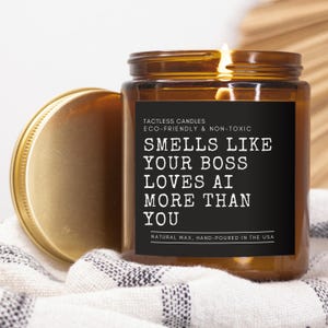 May include: A brown glass candle with a black label that reads "TACTLESS CANDLES ECO-FRIENDLY & NON-TOXIC SMELLS LIKE YOUR BOSS LOVES AI MORE THAN YOU NATURAL WAX, HAND-POURED IN THE USA".