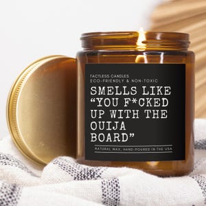 Könnte beinhalten: Eine braune Glaskerze mit einem schwarzen Etikett, auf dem steht: "TACTLESS CANDLES ECO-FRIENDLY & NON-TOXIC SMELLS LIKE "YOU F*CKED UP WITH THE OUIJA BOARD" NATURAL WAX, HAND-POURED IN THE USA".