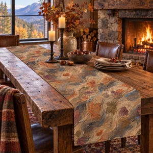 Peut inclure: Un chemin de table rectangulaire présentant un motif marbré tourbillonnant dans des tons de brun, orange, bleu et vert, agrémenté de motifs de feuilles d'automne éparpillés. Le tissu présente un aspect tissé texturé posé sur une table en bois.