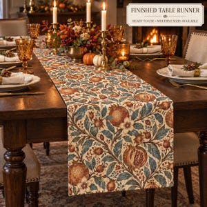 May include: A table runner featuring a botanical pattern of pomegranates, flowers, and leaves in shades of rust, blue, and cream. The text FINISHED TABLE RUNNER READY TO USE MULTIPLE SIZES AVAILABLE is printed in the upper right corner of the image.