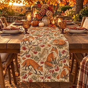 May include: A rectangular table runner featuring a repeating pattern of orange foxes, green foliage, and red berries on a cream background. The fabric displays multiple foxes in various poses, including standing, sitting, and curled up, amidst branches.