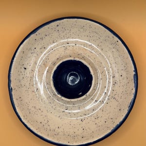 Op de afbeelding: Een witte keramische serveerschaal met een blauwe rand en een blauw midden. De schaal heeft een gespikkeld patroon en is perfect om snacks of dips te serveren.