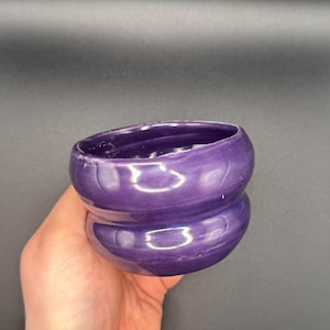 Könnte beinhalten: Eine kleine, violette Keramikschale mit einem abgerundeten, leicht ausgestellten Rand. Die Schale hat eine glänzende Oberfläche und ein subtiles Wirbelmuster.