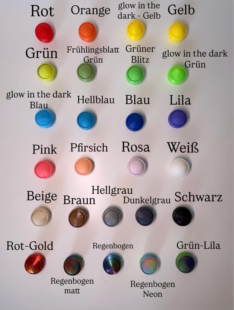 May include: A collection of twenty-six circular buttons arranged in a grid, featuring a wide variety of solid colors, glow-in-the-dark options, metallic finishes, and rainbow gradients, each labeled with its corresponding color name in German text.