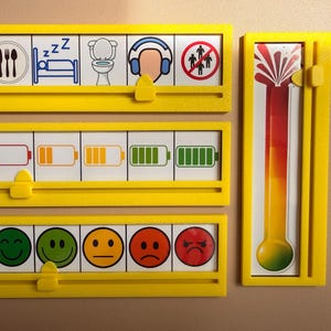 May include: Three horizontal yellow plastic frames with sliding tabs and one vertical yellow frame with a sliding tab. The frames contain visual communication cards showing daily activities, battery charge levels, emotional faces, and a color-coded thermometer.
