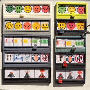 Peut inclure: Une collection de réglettes coulissantes en plastique rectangulaires présentant diverses icônes, notamment des émojis, des niveaux de batterie, des activités quotidiennes et des volcans. Chaque réglette possède un curseur mobile pour indiquer un choix.
