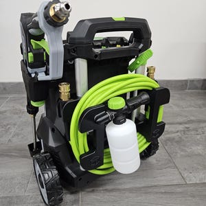 May include: A black and green pressure washer with a gray handle and nozzle. A coiled green hose is attached, along with a white soap dispenser. The pressure washer has two wheels for easy movement.