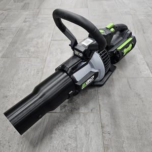 May include: A black and gray leaf blower with a curved handle and a long nozzle. The blower has green accents and the text "EGO COMMERCIAL". The blower is on a gray tiled surface.