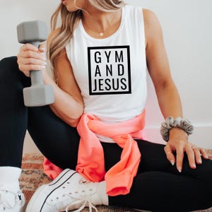 Puede incluir: Camiseta blanca sin mangas con texto negro que dice "GYM AND JESUS" en un cuadro.