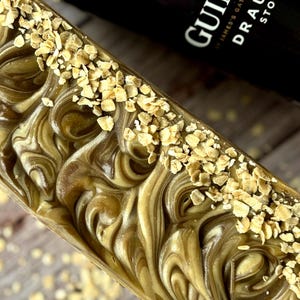 Peut inclure: Un pain de savon artisanal avec un motif tourbillonnant de couleurs marron et cr&egrave;me, parsem&eacute; de flocons d'avoine. Le savon a un aspect rustique et naturel, sugg&eacute;rant une composition &agrave; base d'ingr&eacute;dients biologiques.