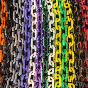 May include: A close-up view of colorful chains arranged vertically. The chains display a spectrum of colors, including orange, black, gray, purple, green, yellow, red, and blue. The links are uniform in size and shape, creating a visually striking pattern.