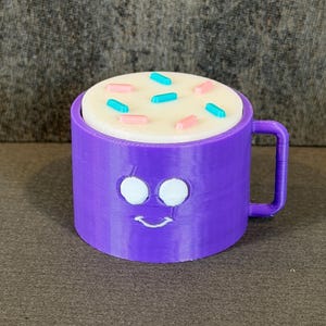 May include: A purple mug with a smiling face design, filled with a white substance and topped with pink and blue sprinkles. The mug has a handle and is sitting on a brown surface.