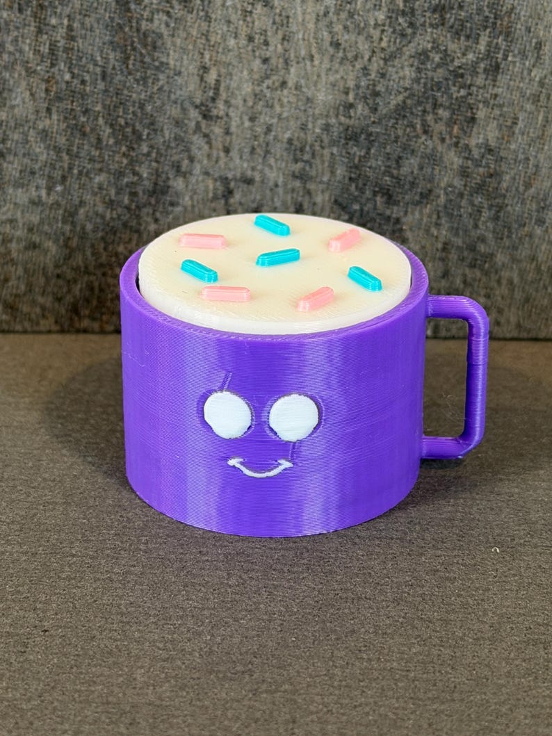 May include: A purple mug with a smiling face design, filled with a white substance and topped with pink and blue sprinkles. The mug has a handle and is sitting on a brown surface.