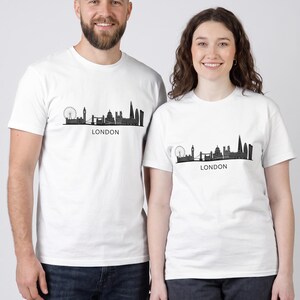Peut inclure: Un t-shirt blanc à manches courtes orné d'une illustration graphique noire de la ligne d'horizon de Londres, incluant le London Eye, Big Ben et le Tower Bridge, avec le mot LONDON imprimé en lettres capitales noires sous le dessin.