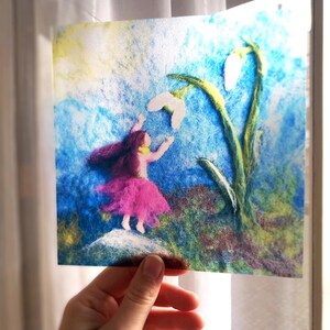 May include: A square needle felted art piece depicting a figure with long dark hair wearing a pink skirt, reaching towards two white snowdrop flowers. The background features blended shades of blue, green, and yellow fibres on a textured surface.