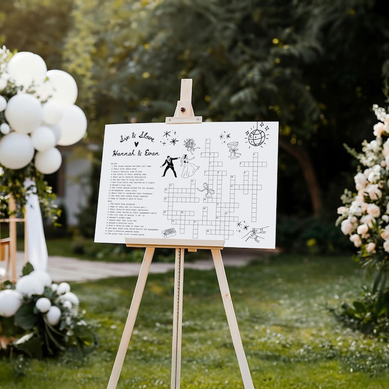 May include: A white sign on a wooden easel with the words "Sip & Solve" and "Hannah & Evan" in black script. The sign features a crossword puzzle with wedding-themed clues and illustrations. The easel is made of light-colored wood and is set outdoors.