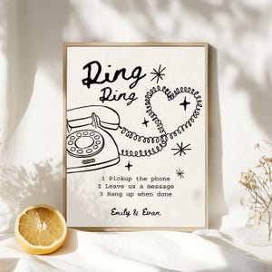 May include: A framed print with a retro design. The artwork features a vintage telephone illustration, the words "Ring Ring", and instructions. The phone cord forms a heart shape. The names "Emily & Evan" are at the bottom. A sliced lemon is in the foreground.