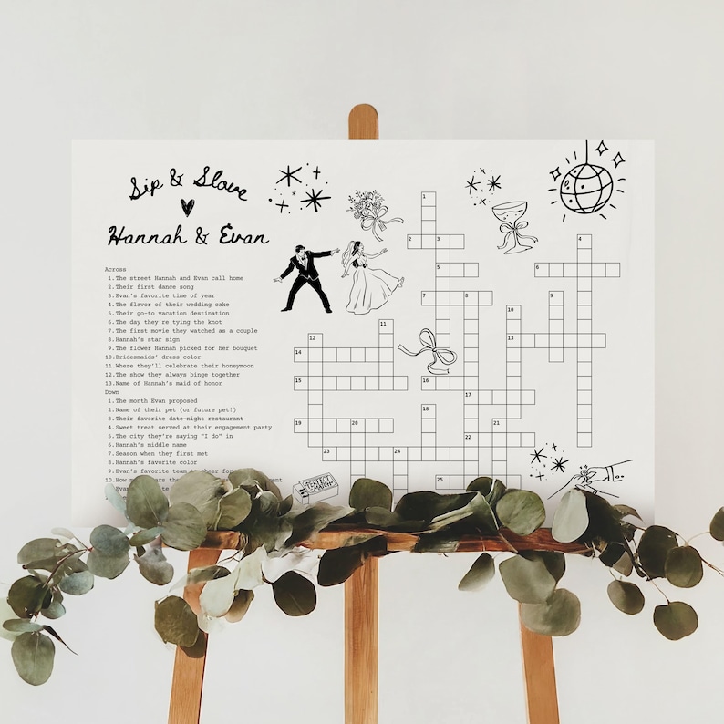 May include: A white wedding crossword puzzle sign with the names "Hannah & Evan" in script. The sign includes a crossword puzzle with clues, illustrations of a bride and groom, and decorative elements.
