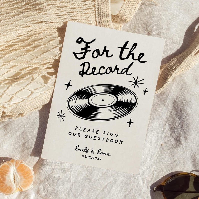 May include: A white sign with black text and a black and white illustration of a vinyl record. The text reads "For the Record" and "Please sign our guestbook." The sign also includes the names "Emily & Evan" and the date "09.12.20XX".