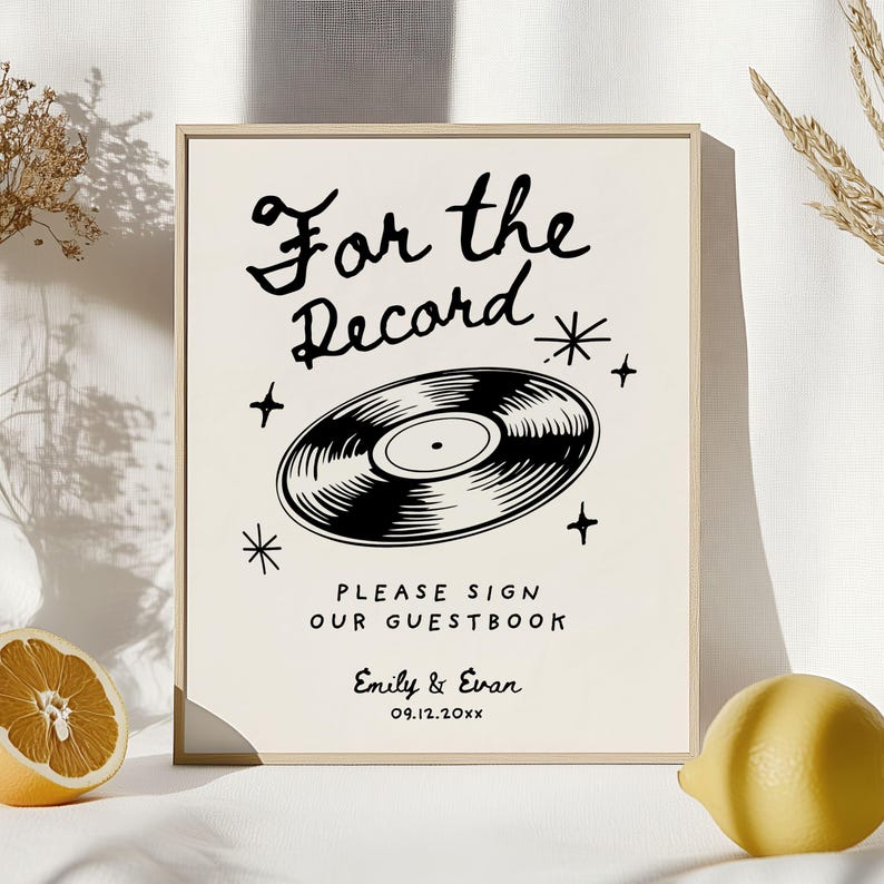 May include: A white sign with a black vinyl record illustration and the text "For the Record". Below the record is the text "Please sign our guestbook" and the names "Emily & Evan" with the date "09.12.20xx".