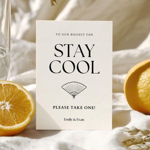 K&ouml;nnte beinhalten: Eine cremefarbene Karte mit den Worten "STAY COOL" in fetter schwarzer Schrift und einer F&auml;cherillustration. Die Karte lautet "TO OUR BIGGEST FAN" und "PLEASE TAKE ONE!" mit den Namen "Emily & Evan" unten. Auf beiden Seiten sind Orangenscheiben.