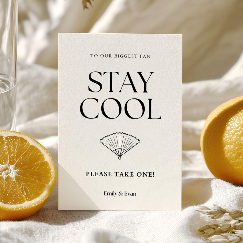 K&ouml;nnte beinhalten: Eine cremefarbene Karte mit den Worten "STAY COOL" in fetter schwarzer Schrift und einer F&auml;cherillustration. Die Karte lautet "TO OUR BIGGEST FAN" und "PLEASE TAKE ONE!" mit den Namen "Emily & Evan" unten. Auf beiden Seiten sind Orangenscheiben.