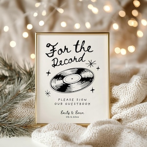 May include: A white sign with a gold frame, featuring a black and white illustration of a vinyl record with the text "For the Record" and "Please sign our guestbook". The sign also includes the names "Emily & Evan" and the date "09.12.20XX".